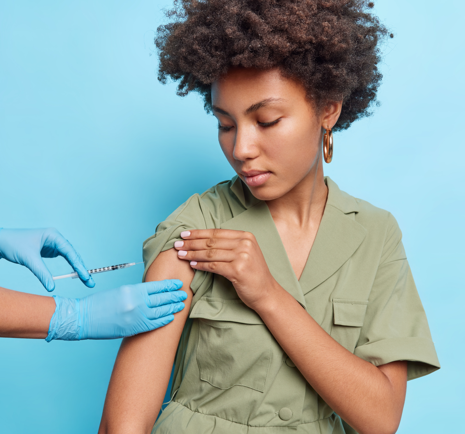serious-woman-with-curly-hair-gets-injection-vaccine-against-coronavirus-disease-wears-green-dress-isolated-blue-wall 1